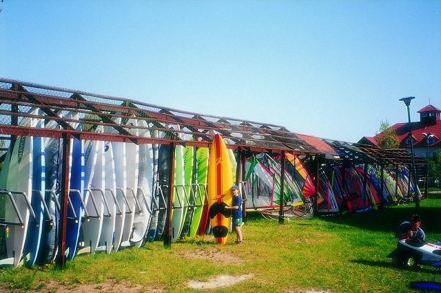 Wypoyczalnia i przechowalnia sprztu windsurfingowego. Wida pierwszy rzd desek (za nim jest drugi), na dalszym planie wieszaki na agle. Kada deska jest zamykana na oddzieln kdk, a kady wczasowicz ma klucz do swojej deski. Sprzt jest pilnowany w dzie i w nocy. 